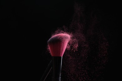Photo of Makeup brushes with pink eye shadow on black background, closeup