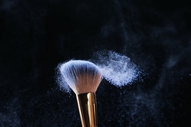 Photo of Makeup brush with cosmetic product on black background, closeup