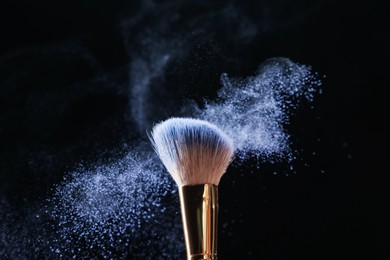 Photo of Makeup brush with cosmetic product on black background, closeup