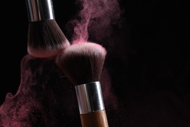 Photo of Makeup brushes with color eye shadow on black background, closeup