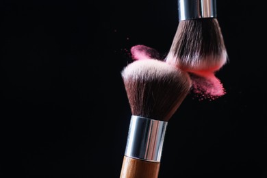Photo of Makeup brushes with color eye shadow on black background, closeup