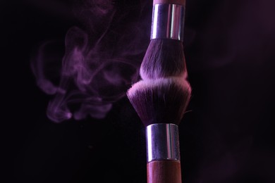 Photo of Makeup brushes with purple eye shadow in neon lights on black background, closeup. Space for text