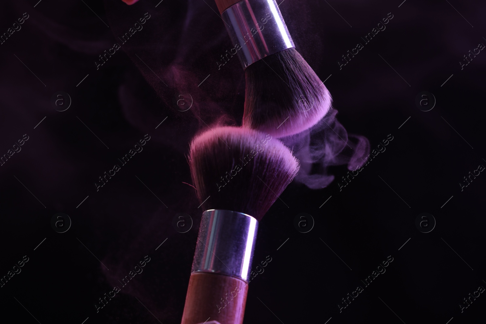 Makeup brushes with purple eye shadow in neon lights on black background, closeup Photo of Makeup brushes with purple eye shadow in neon lights on black background, closeup