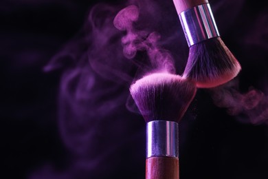 Photo of Makeup brushes with purple eye shadow in neon lights on black background, closeup. Space for text