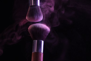Photo of Makeup brushes with purple eye shadow in neon lights on black background, closeup. Space for text