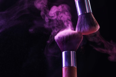 Photo of Makeup brushes with purple eye shadow in neon lights on black background, closeup. Space for text