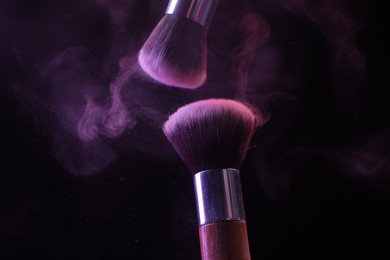 Photo of Makeup brushes with purple eye shadow in neon lights on black background, closeup