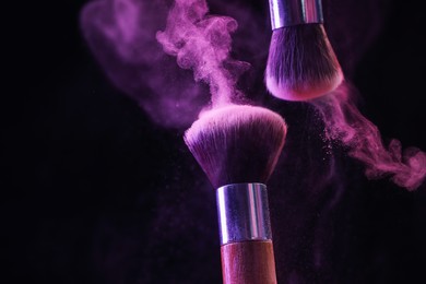 Photo of Makeup brushes with colorful eye shadows in neon lights on black background, closeup. Space for text