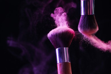 Photo of Makeup brushes with colorful eye shadows in neon lights on black background, closeup. Space for text