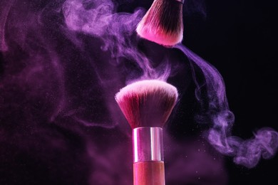 Photo of Makeup brushes with colorful eye shadows in neon lights on black background, closeup