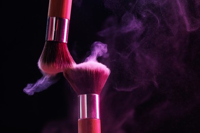 Photo of Makeup brushes with colorful eye shadows in neon lights on black background, closeup