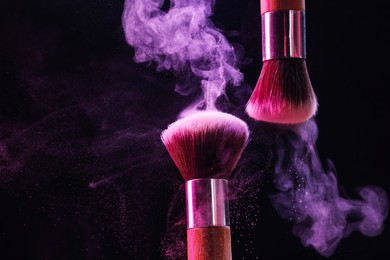 Photo of Makeup brushes with colorful eye shadows in neon lights on black background, closeup