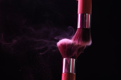 Photo of Makeup brushes with pink eye shadow on black background, closeup. Space for text