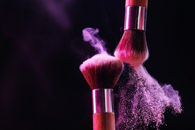 Photo of Makeup brushes with colorful eye shadows in neon lights on black background, closeup
