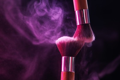 Photo of Makeup brushes with color eye shadow in neon lights on black background, closeup. Space for text