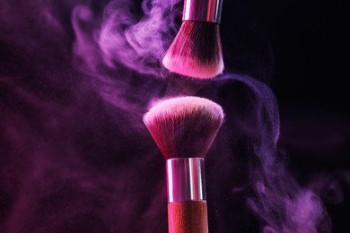 Photo of Makeup brushes with colorful eye shadows in neon lights on black background, closeup