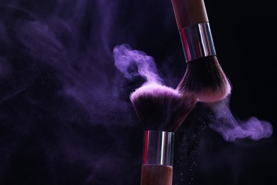 Photo of Makeup brushes with purple eye shadow in neon lights on black background, closeup. Space for text