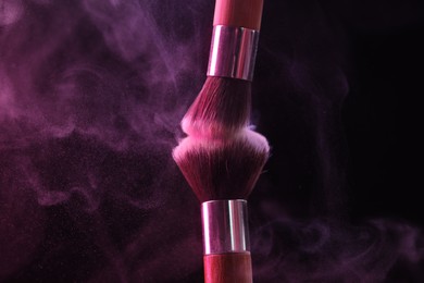 Photo of Makeup brushes with pink eye shadow on black background, closeup