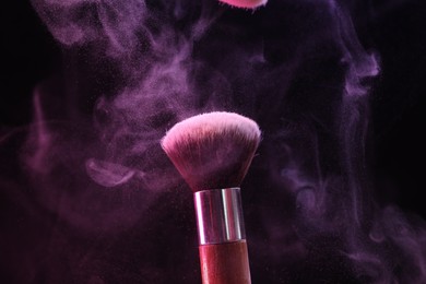 Photo of Makeup brush with color eye shadow in neon lights on black background, closeup