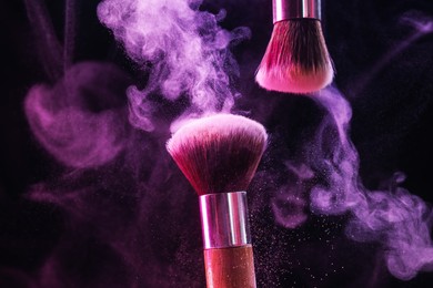 Photo of Makeup brushes with colorful eye shadows in neon lights on black background, closeup