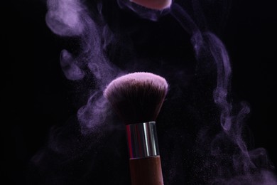 Photo of Makeup brush with purple eye shadow on black background, closeup