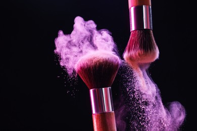 Photo of Makeup brushes with color eye shadow in neon lights on black background, closeup