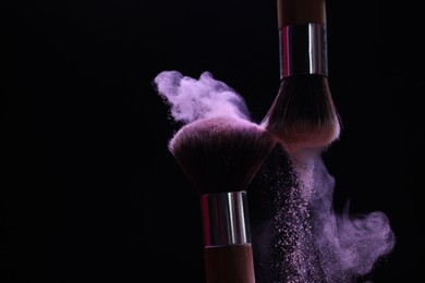 Photo of Makeup brushes with purple eye shadow on black background, closeup