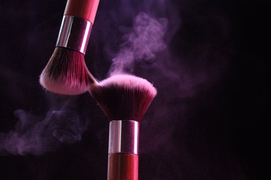 Photo of Makeup brushes with color eye shadow on black background, closeup