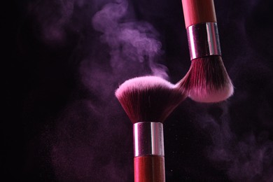 Photo of Makeup brushes with color eye shadow on black background, closeup