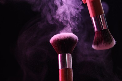 Photo of Makeup brushes with color eye shadow on black background, closeup