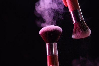 Photo of Makeup brushes with color eye shadow on black background, closeup