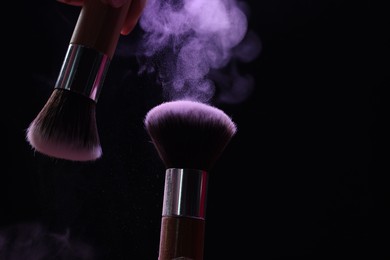 Photo of Makeup brushes with purple eye shadow on black background, closeup