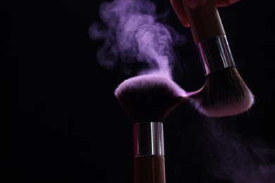 Photo of Makeup brushes with purple eye shadow on black background, closeup