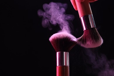 Photo of Makeup brushes with color eye shadow on black background, closeup. Space for text
