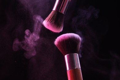 Photo of Makeup brushes with color eye shadow on black background, closeup