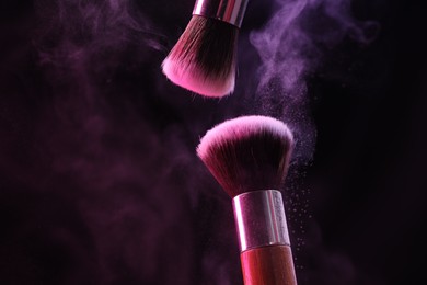 Photo of Makeup brushes with colorful eye shadows in neon lights on black background, closeup