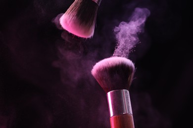 Photo of Makeup brushes with colorful eye shadows in neon lights on black background, closeup