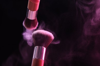 Photo of Makeup brushes with pink eye shadow in neon light on black background, closeup. Space for text