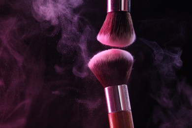 Photo of Makeup brushes with colorful eye shadows in neon lights on black background, closeup. Space for text