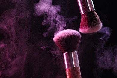 Photo of Makeup brushes with colorful eye shadows in neon lights on black background, closeup. Space for text