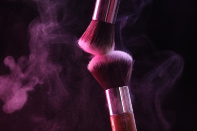 Photo of Makeup brushes with colorful eye shadows in neon lights on black background, closeup