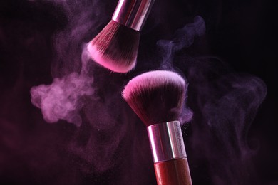 Photo of Makeup brushes with colorful eye shadows in neon lights on black background, closeup