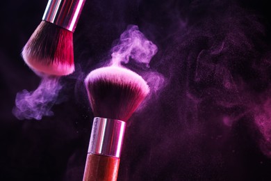 Photo of Makeup brushes with colorful eye shadows in neon lights on black background, closeup. Space for text