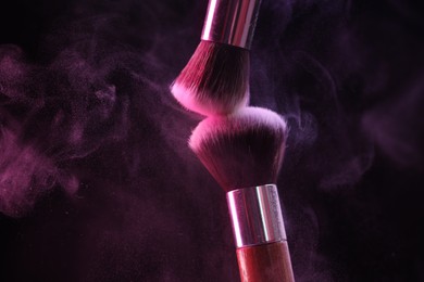 Photo of Makeup brushes with colorful eye shadows in neon lights on black background, closeup. Space for text