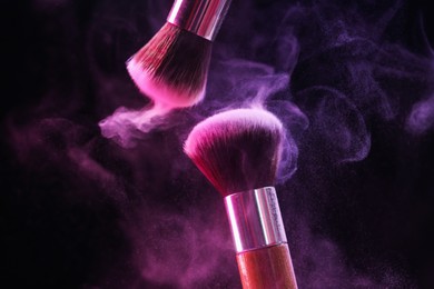 Photo of Makeup brushes with colorful eye shadows in neon lights on black background, closeup