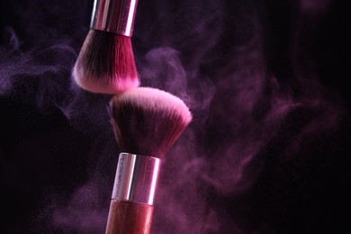 Photo of Makeup brushes with colorful eye shadows in neon lights on black background, closeup. Space for text