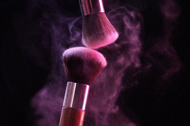 Photo of Makeup brushes with color eye shadow in neon lights on black background, closeup