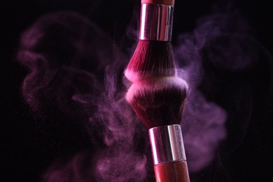Photo of Makeup brushes with color eye shadow in neon lights on black background, closeup