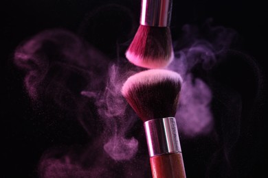 Photo of Makeup brushes with color eye shadow in neon lights on black background, closeup