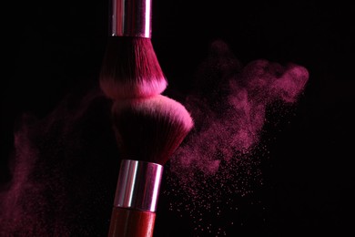 Photo of Makeup brushes with pink eye shadow on black background, closeup. Space for text